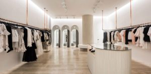 Aje fashion retail store designed using hanging brass pips for clothing, hardwood floors and a white feature column. 