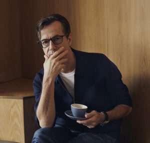 Mark Landini, Creative Director for Landini Associates, in the thinking man pose with a cup of coffee against a wooden background