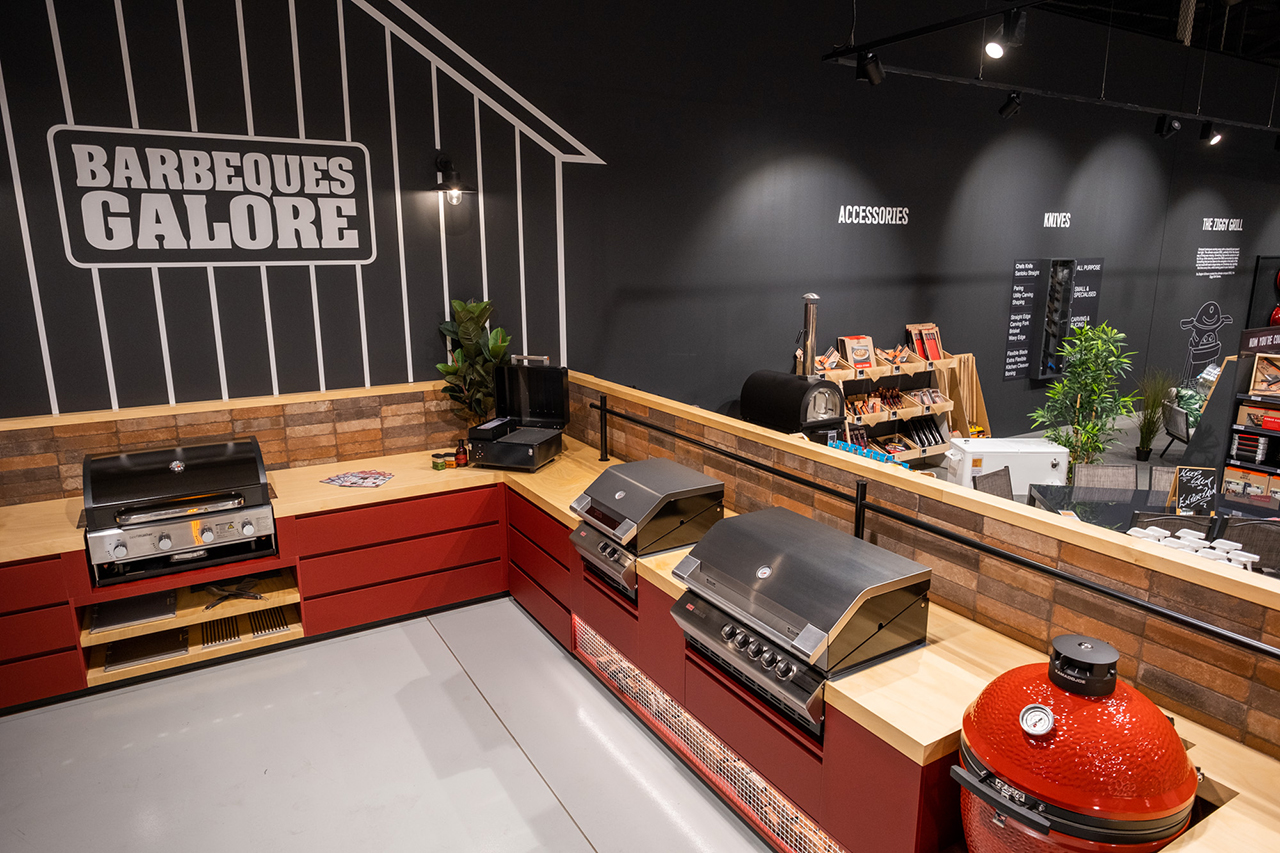 Barbecue store display with built-in grills, red cabinetry, and a black wall sign reading "BARBECUES GALORE."