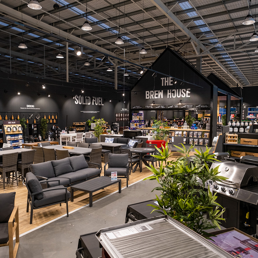 Large retail space displaying outdoor furniture, grills, and signs for "SOLID FUEL" and "THE BREW HOUSE."