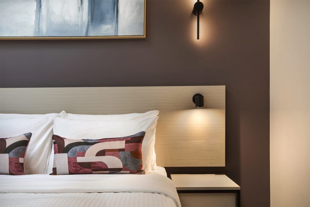 Custom guest room joinery and styling detail at Wanneroo Tavern featuring a timber headboard, integrated reading lights, feature artwork and contemporary accommodation interiors delivered by Unita Australia.