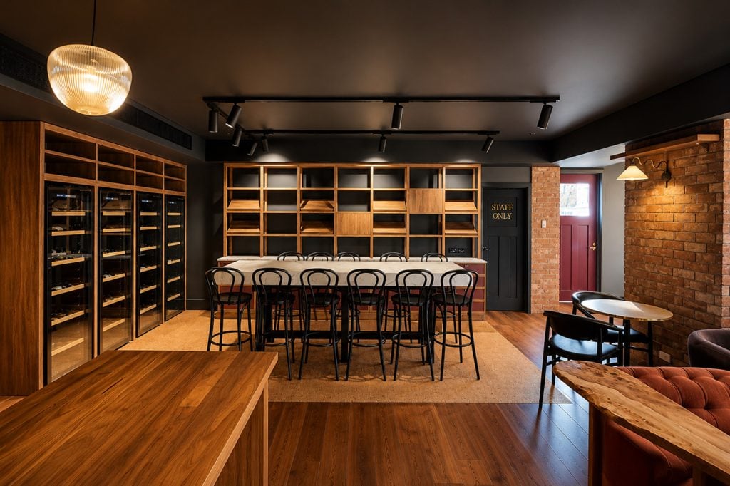 Annibell’s Wine Bar interior featuring timber wine storage, exposed brick walls, warm lighting and a central communal tasting table.